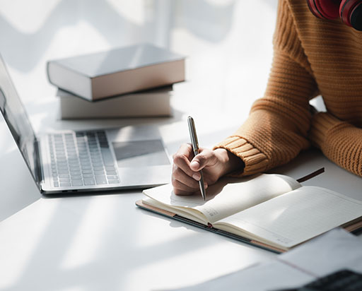 a person sitting by a laptop and writing in a notebook
