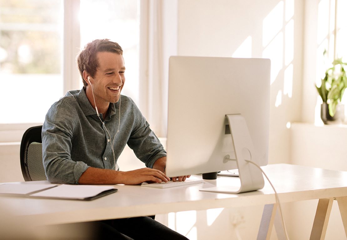 Smiling student with ear buds sitting at home computer