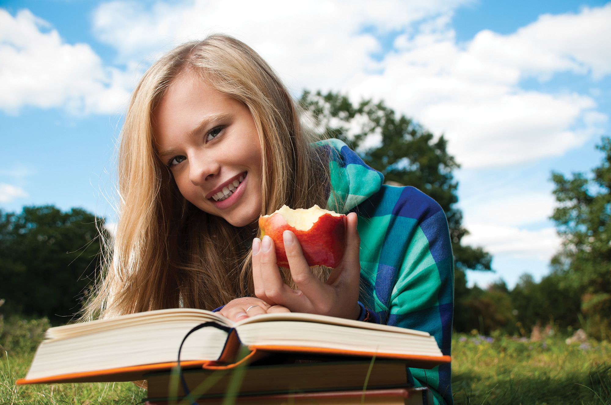 Smiling student sitting in grass and holding an apple