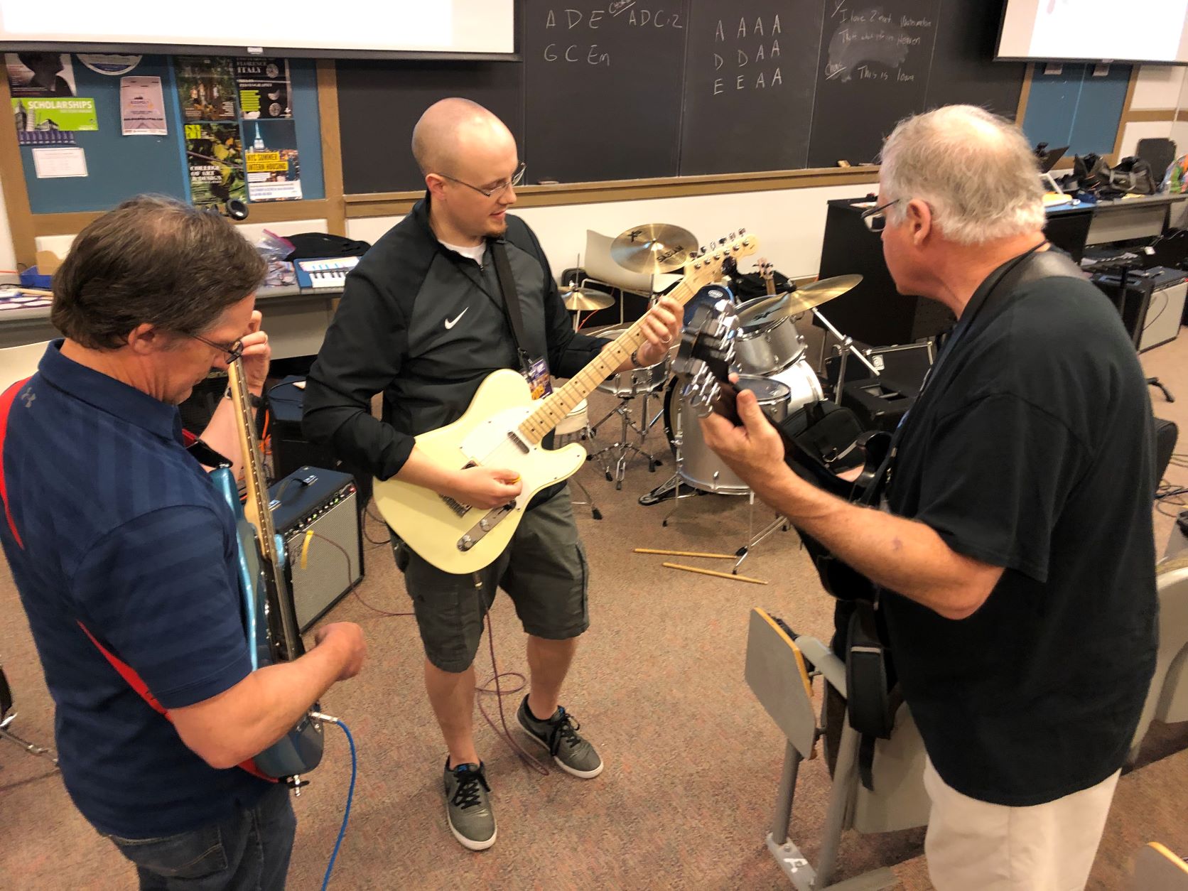 Two workshop participants working with the instructor learning how to play electric guitar
