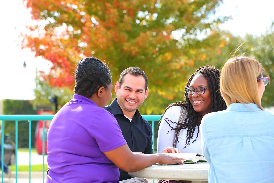 Smiling students sitting outside with staff member