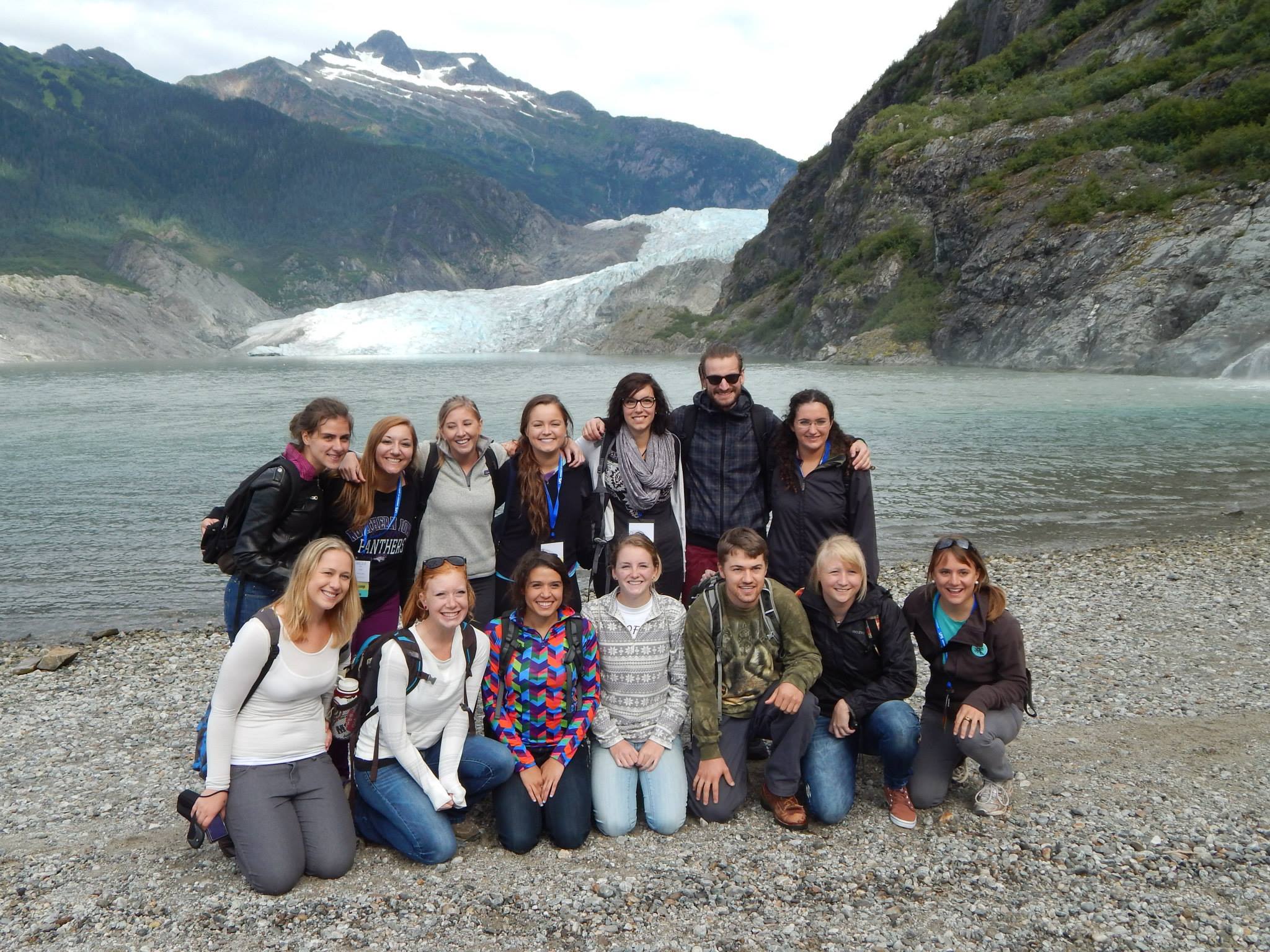 Group of students posing in front of water and a glacier
