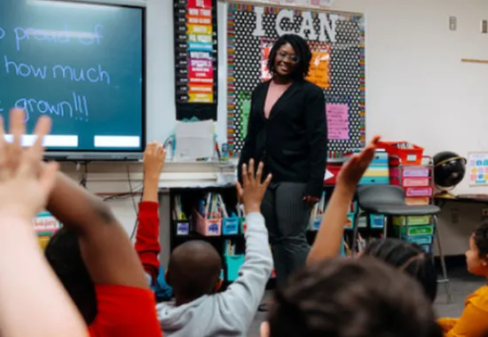 Teacher standing in front of class with hands raised.