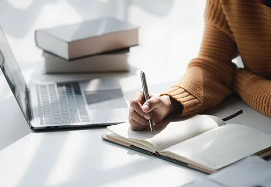 a person sitting by a laptop and writing in a notebook
