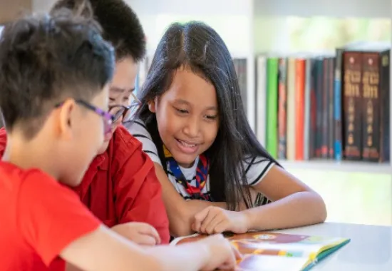 Three children reading from a book together.