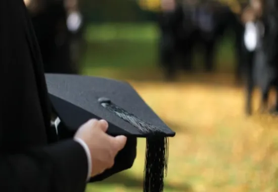 Hands holding a black mortarboard.