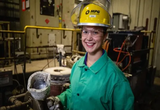Woman in a hard hat and safety glasses doing metal work.