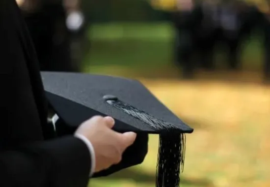 Hands holding a black mortarboard.