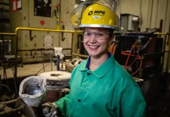 Woman in a hard hat and safety glasses doing metal work.